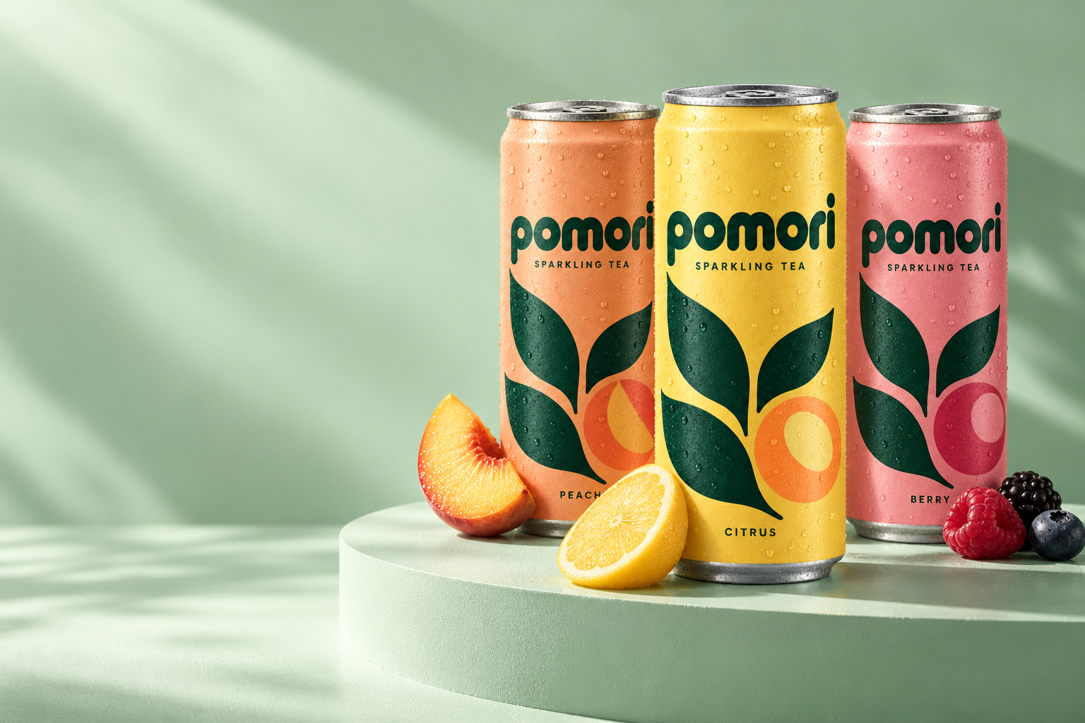 Peach, citrus and berry POMORI cans on a pale mint stage beside a peach slice, half a lemon and fresh berries